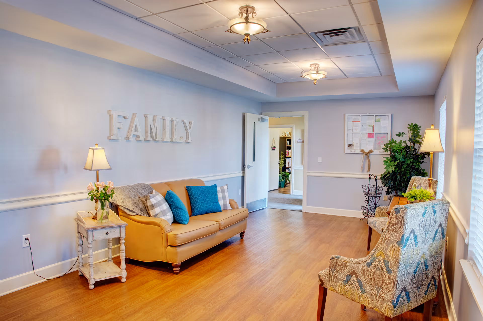 Comfortable seating area with a tan sofa, patterned chairs, side tables and lamps under a 'FAMILY' wall sign.