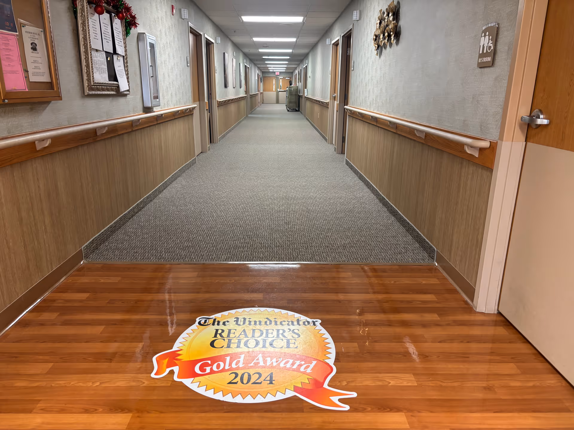 Long interior corridor of Masternick Memorial with handrails along the walls and a 'Reader's Choice Gold Award 2024' floor decal in the foreground.