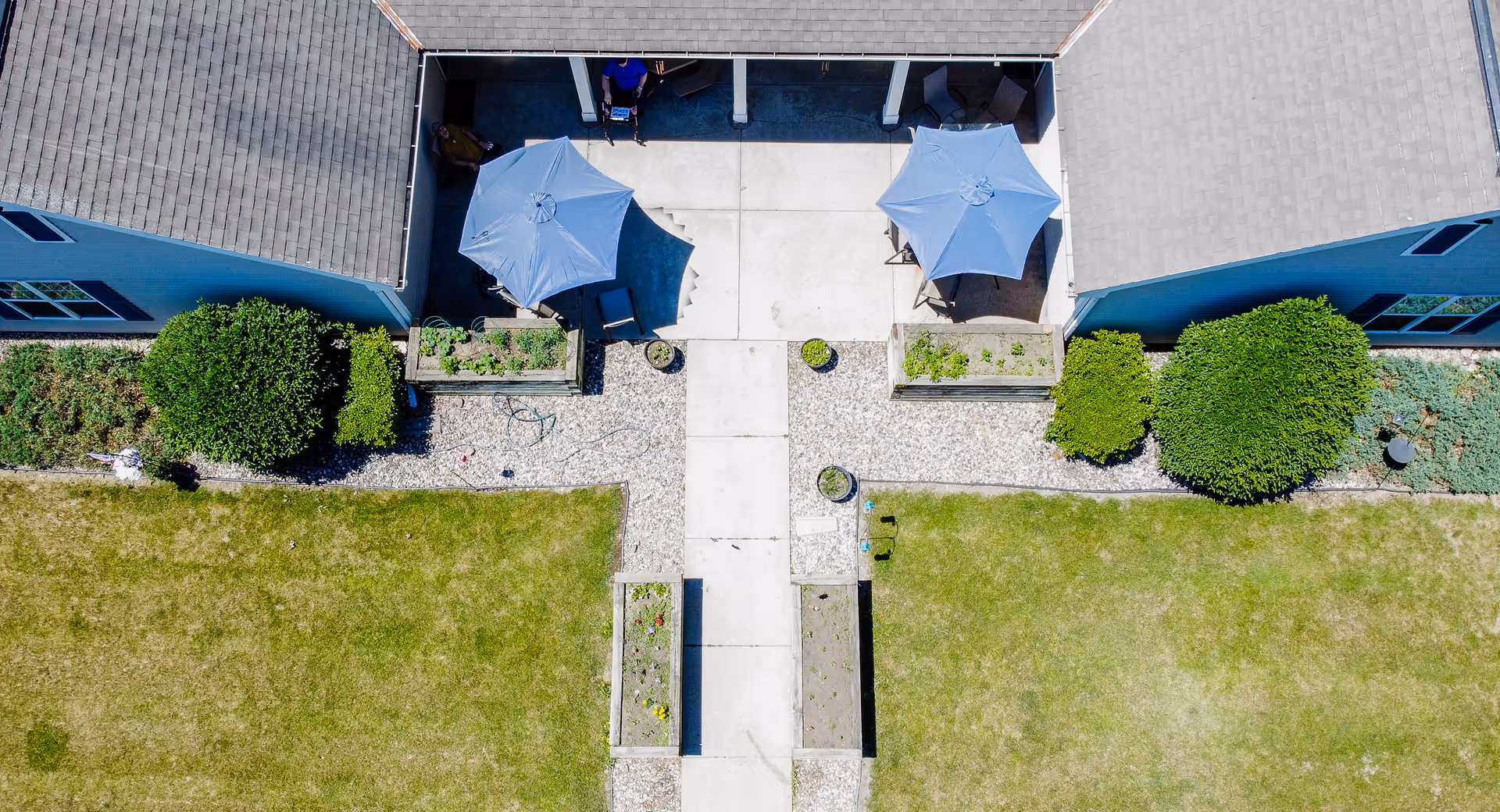 Aerial view of a residential courtyard with two patio umbrellas, walkways, planter boxes, and grassy lawns between building units.