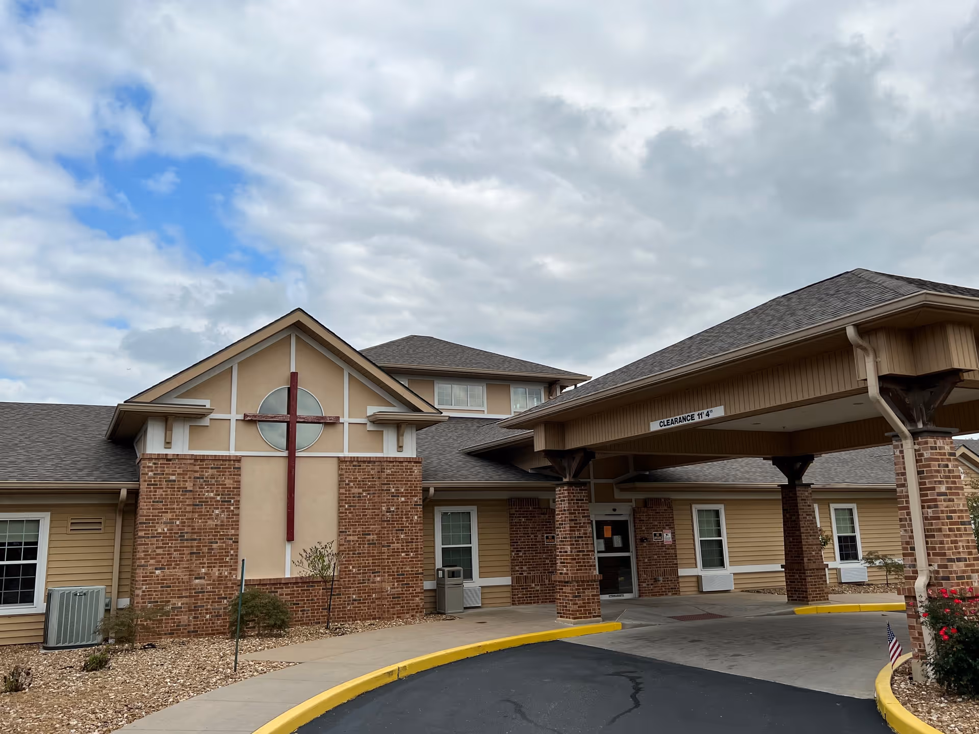 Front entrance of a brick-and-siding nursing facility with a covered drive-through canopy and circular window feature.