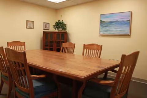 A wooden dining table with chairs in a beige-walled senior living dining room.