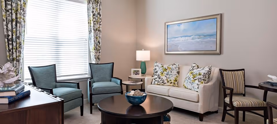 Cozy furnished living room with a white sofa, patterned throw pillows, two armchairs, a round coffee table and wall art.