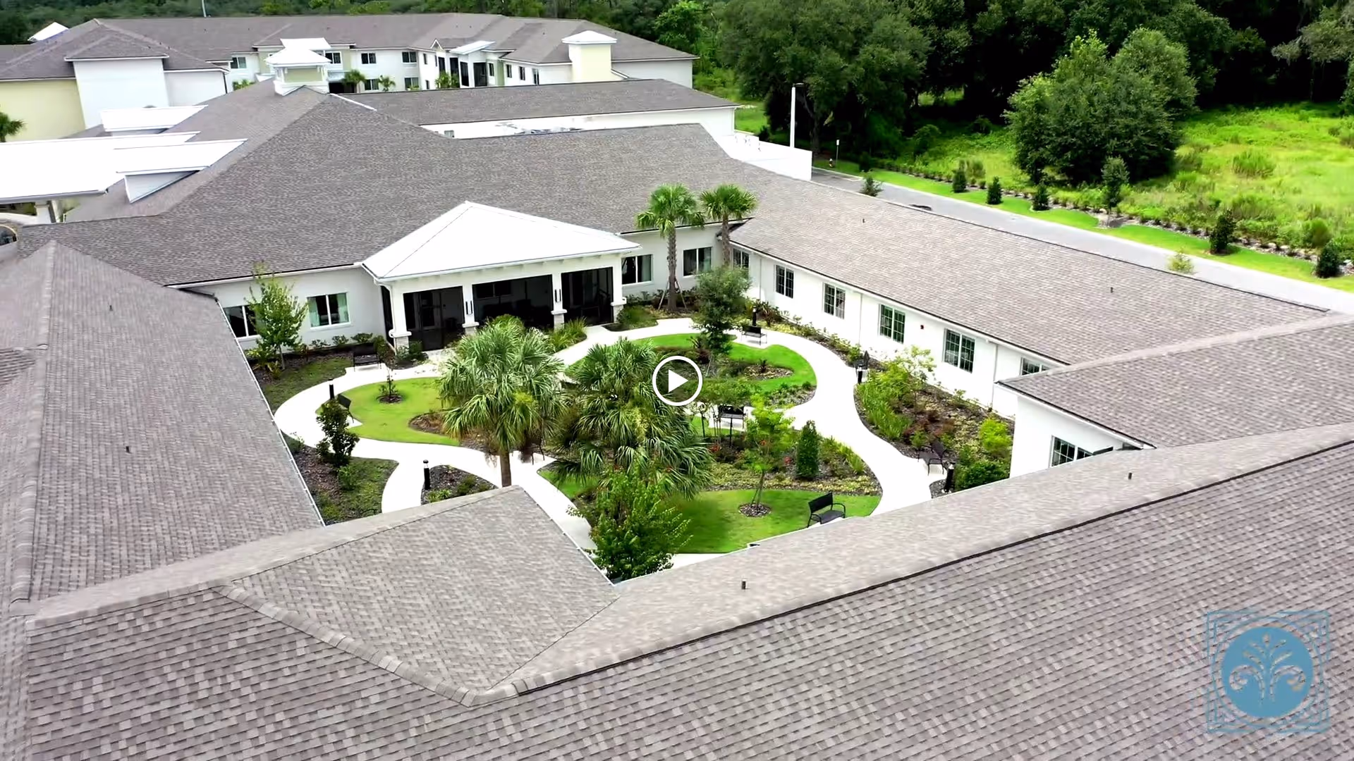 Aerial view of Village Veranda at Lady Lake showing a large building complex with a central courtyard garden featuring pathways, palm trees, benches, and various plants surrounded by the building's roof.