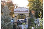 Entrance arch sign reads Grand Pavilion Senior Living, with cars and greenery in front.