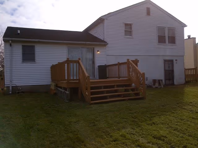 Rear exterior of a white two-story house with a wooden deck and steps leading to a grassy backyard.