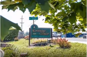 Outdoor view of a green sign for Northridge Center assisted living and memory care, surrounded by landscaping with bushes and trees, with a street sign and power lines visible in the background.