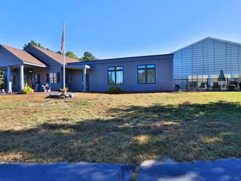 Exterior view of Merrimack Meadows facility with flagpole, lawn, and entrance.