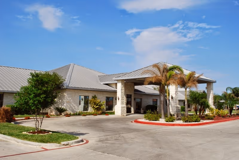 Front entrance of a single-story nursing facility with a covered porte-cochere, palm trees, and a circular driveway under a blue sky.