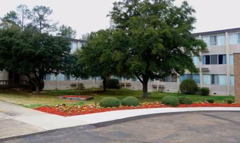 Exterior view of a multi-story senior living facility with trees and landscaped beds.