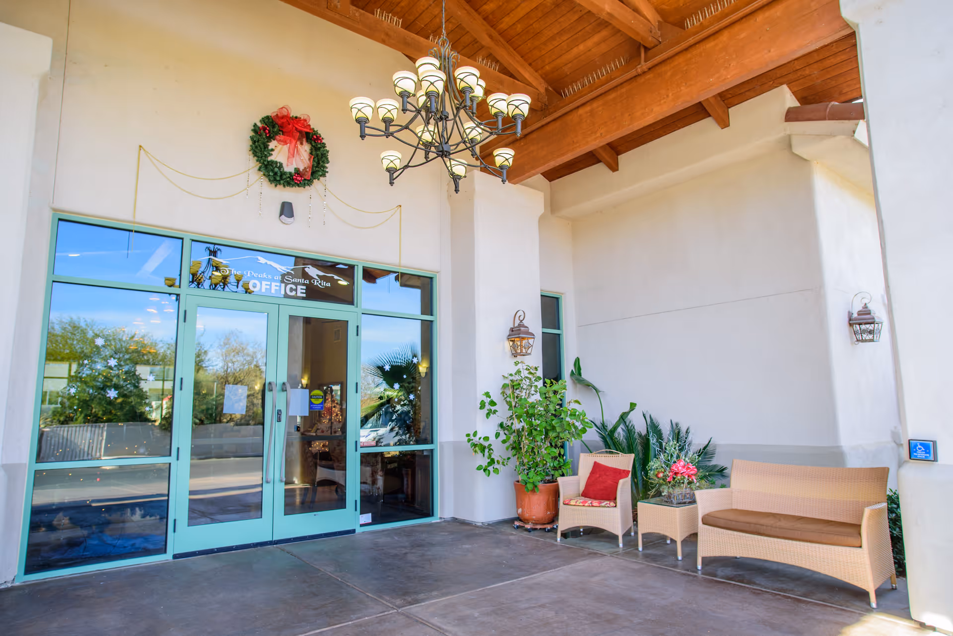 Covered entryway with glass double doors labeled 'Office', wicker seating, potted plants and a hanging chandelier.