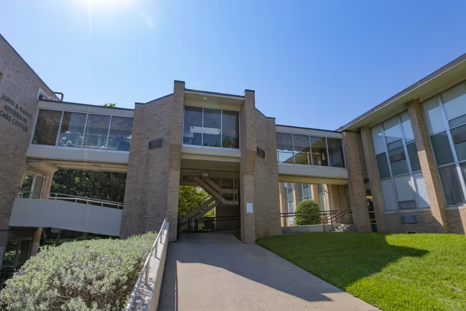 Exterior view of a brick multi‑section senior living building with a covered walkway, ramp, and grassy lawn under a clear blue sky.