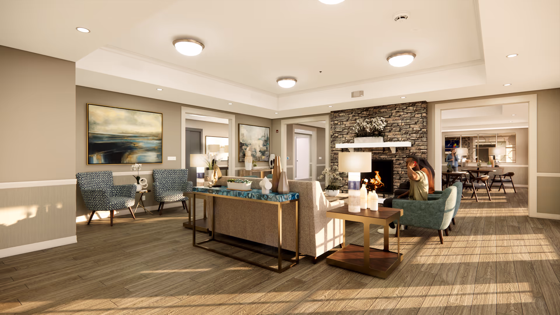 A cozy senior living common area with a stone fireplace, a beige sofa, two blue armchairs, a wooden side table with lamps, and decorative paintings on the walls. Sunlight streams through windows, illuminating the wood flooring and creating a warm atmosphere. In the background, there is a dining area with tables and chairs.