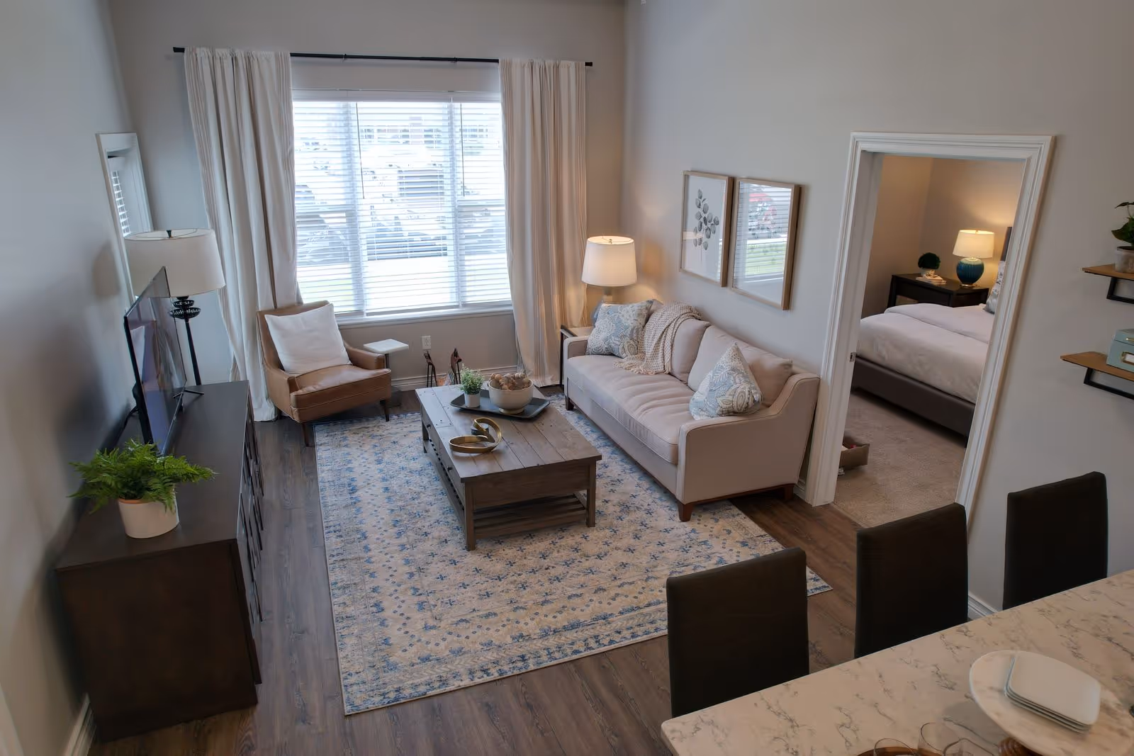 Bright modern living room with a sofa, armchair, coffee table, TV console, and a view into a bedroom.
