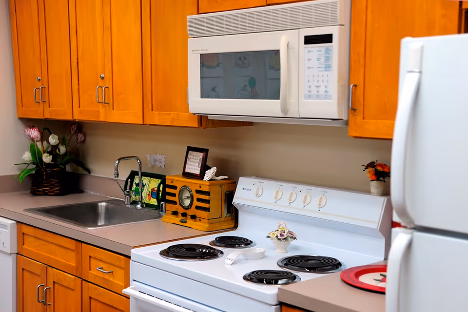 Well-lit kitchen with wooden cabinets, a microwave, stainless sink, electric stove, and a refrigerator.