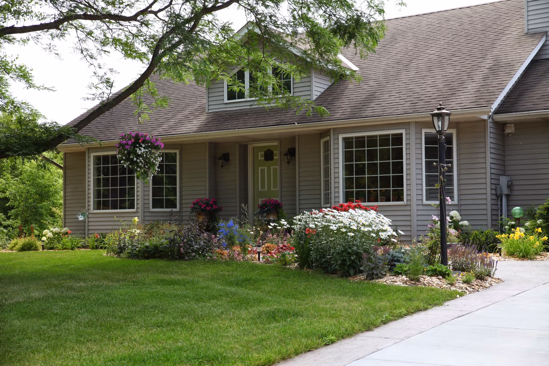 Front exterior of a single-story house with a green door, large windows, a hanging flower basket and a landscaped garden.