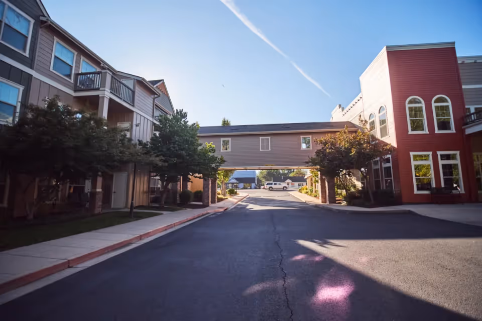 Driveway and skybridge connecting two multi-story residential buildings with trees under a clear blue sky.