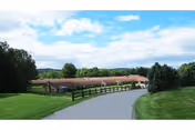 A paved driveway curves down toward a single-story brick health care building set among green lawns, trees, and a partly cloudy sky.
