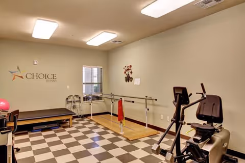 A small senior rehabilitation/exercise room with parallel bars, an exercise bike, a therapy table, and checkered flooring.