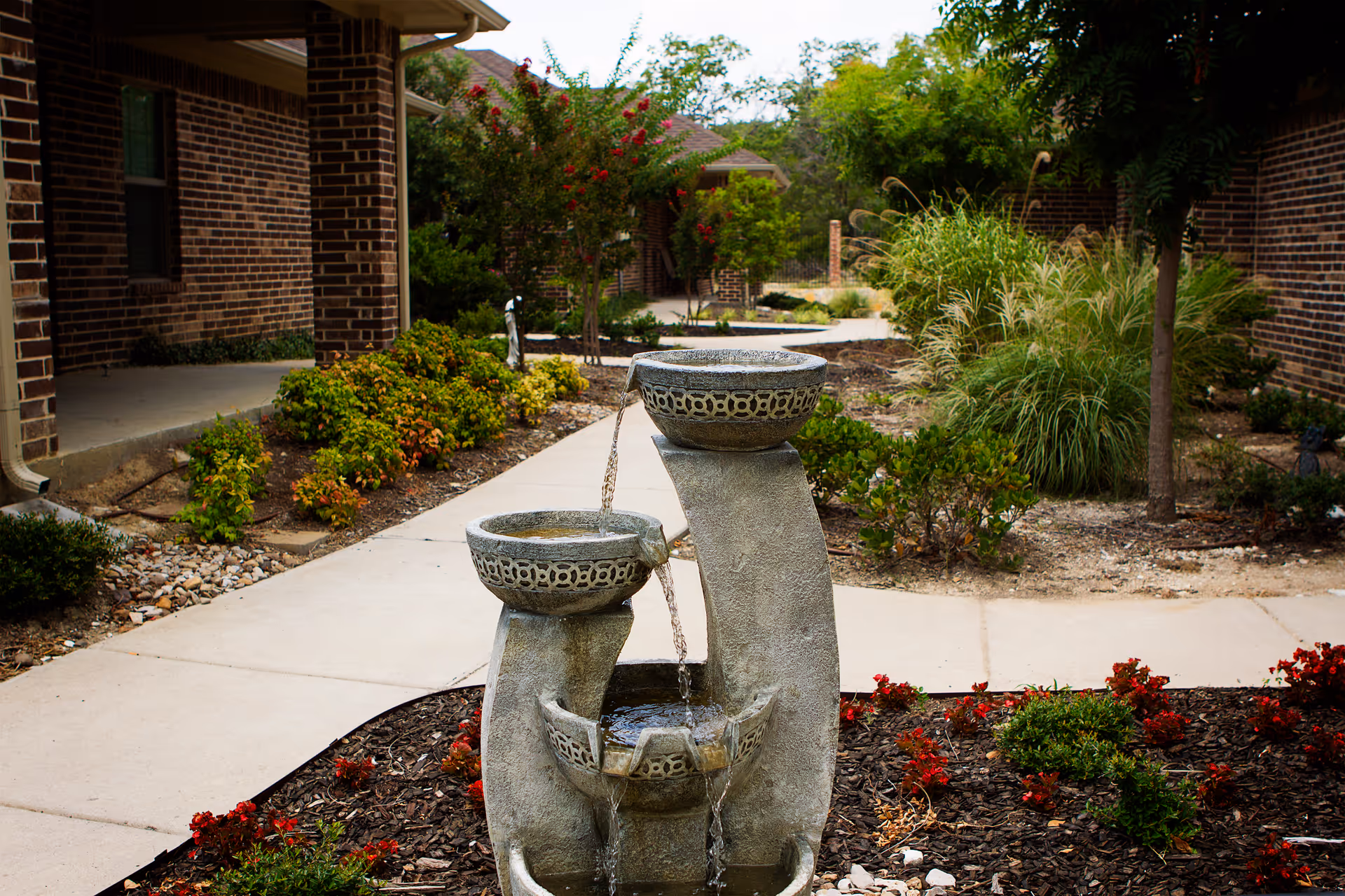 Stone tiered water fountain in a landscaped courtyard with brick assisted living buildings and walkways.
