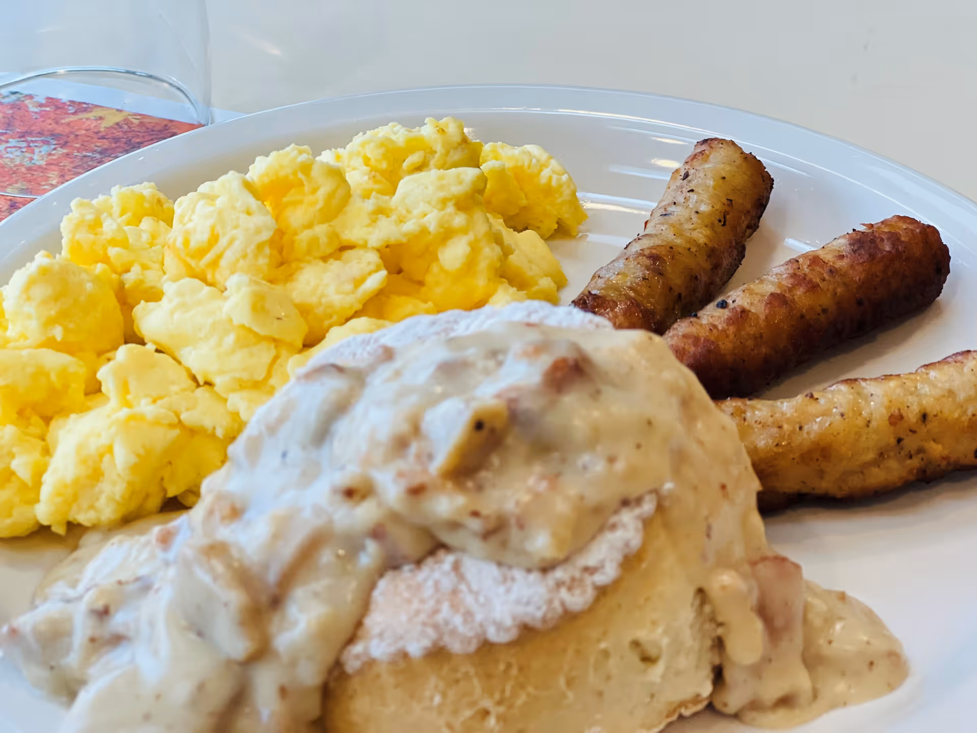 A plate of breakfast food featuring scrambled eggs, three sausage links, and a biscuit topped with creamy sausage gravy.