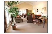 Bright communal living area with several armchairs, side tables, plants, and large windows.