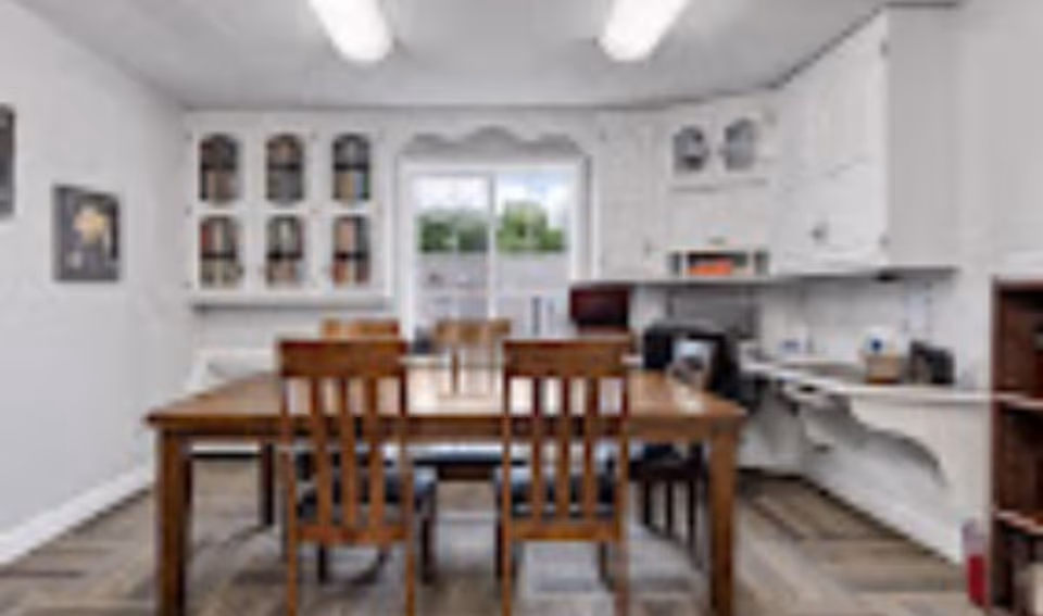 Communal dining room with a wooden table and chairs, white built-in cabinets and a countertop along the right wall.
