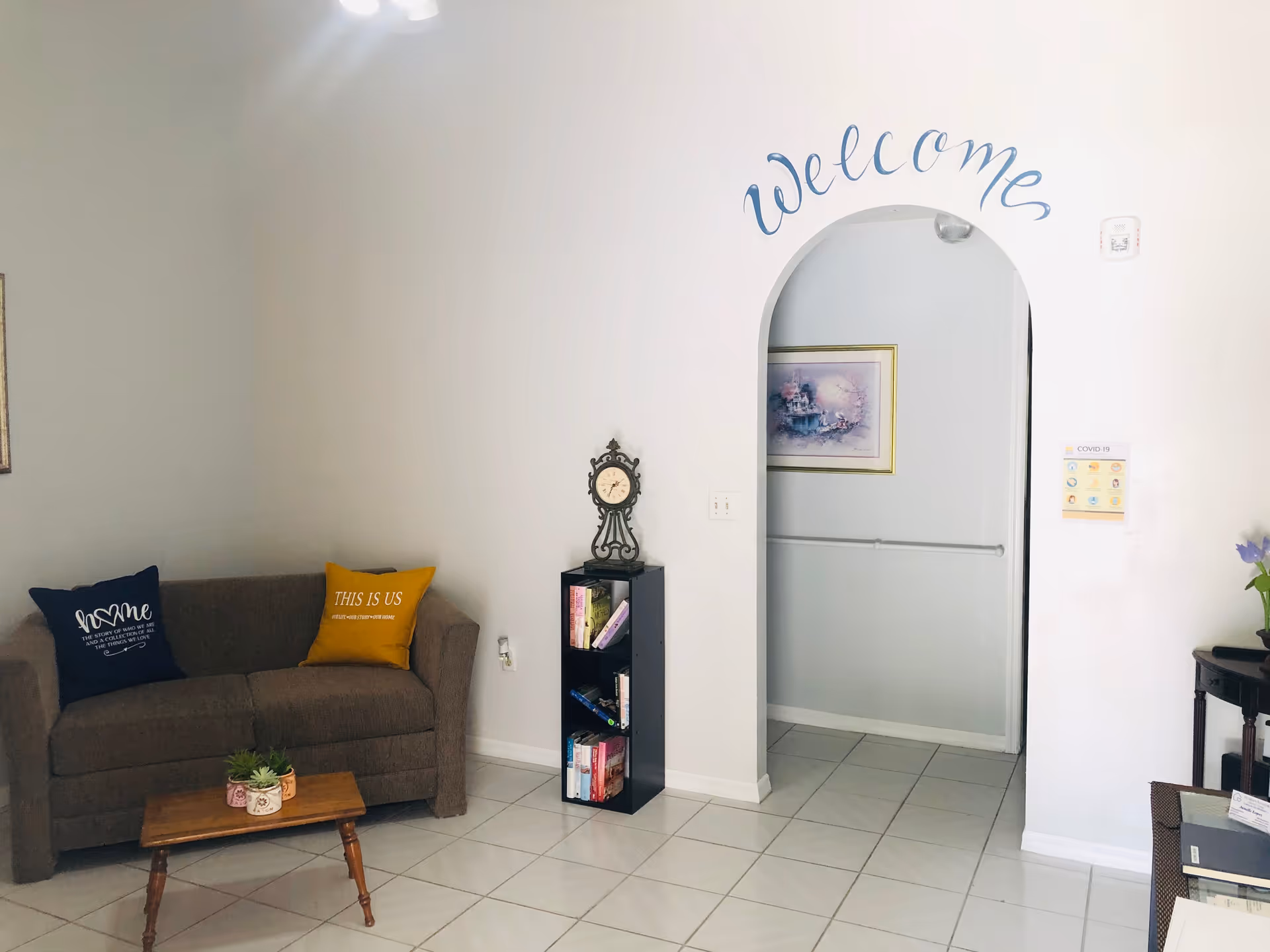 Cozy living area with sofa, coffee table, bookshelf, Welcome arch, and tiled floor.