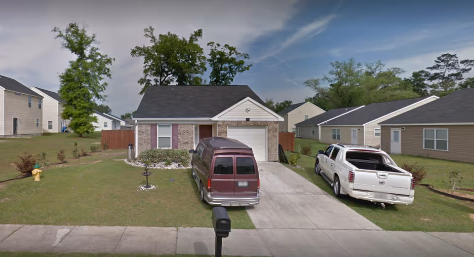 Single-story brick-front house with attached garage, a driveway with two vehicles, front lawn and mailbox.