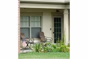 Covered ground-floor patio with two outdoor chairs and a small table in front of a window and door.