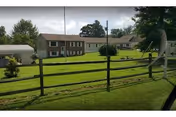Exterior view of Essene Inc facility with green lawn, wooden fence, and residential buildings.