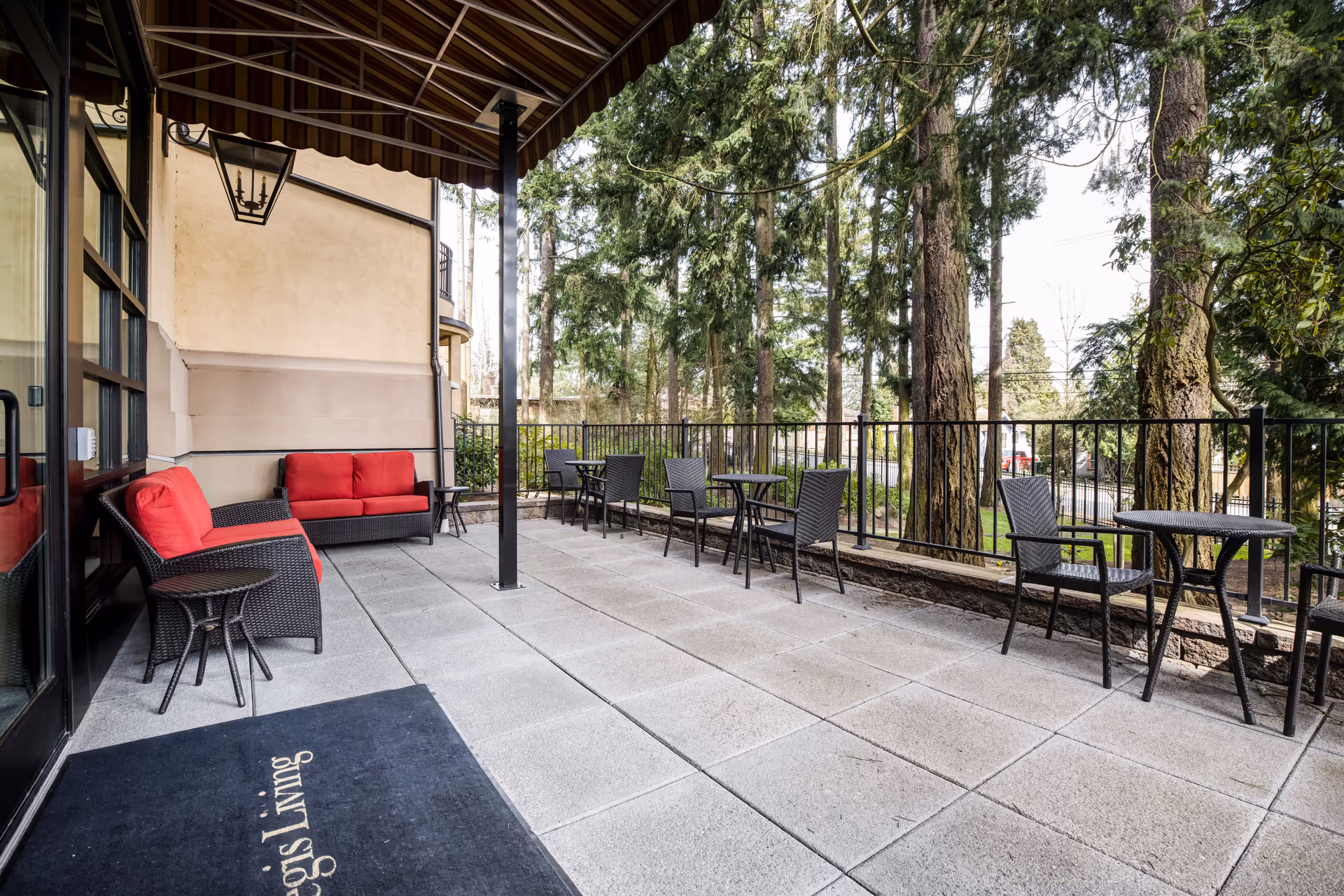 Outdoor patio with wicker chairs and red-cushioned sofas under an awning overlooking trees.
