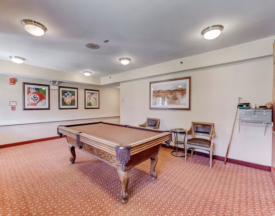 Billiards room with a pool table, chairs, framed artwork, and patterned carpet.
