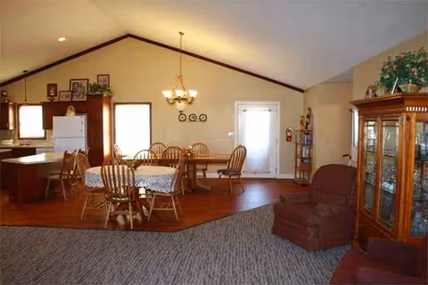 Open-plan dining and living area with wooden chairs, table, and a glass cabinet.