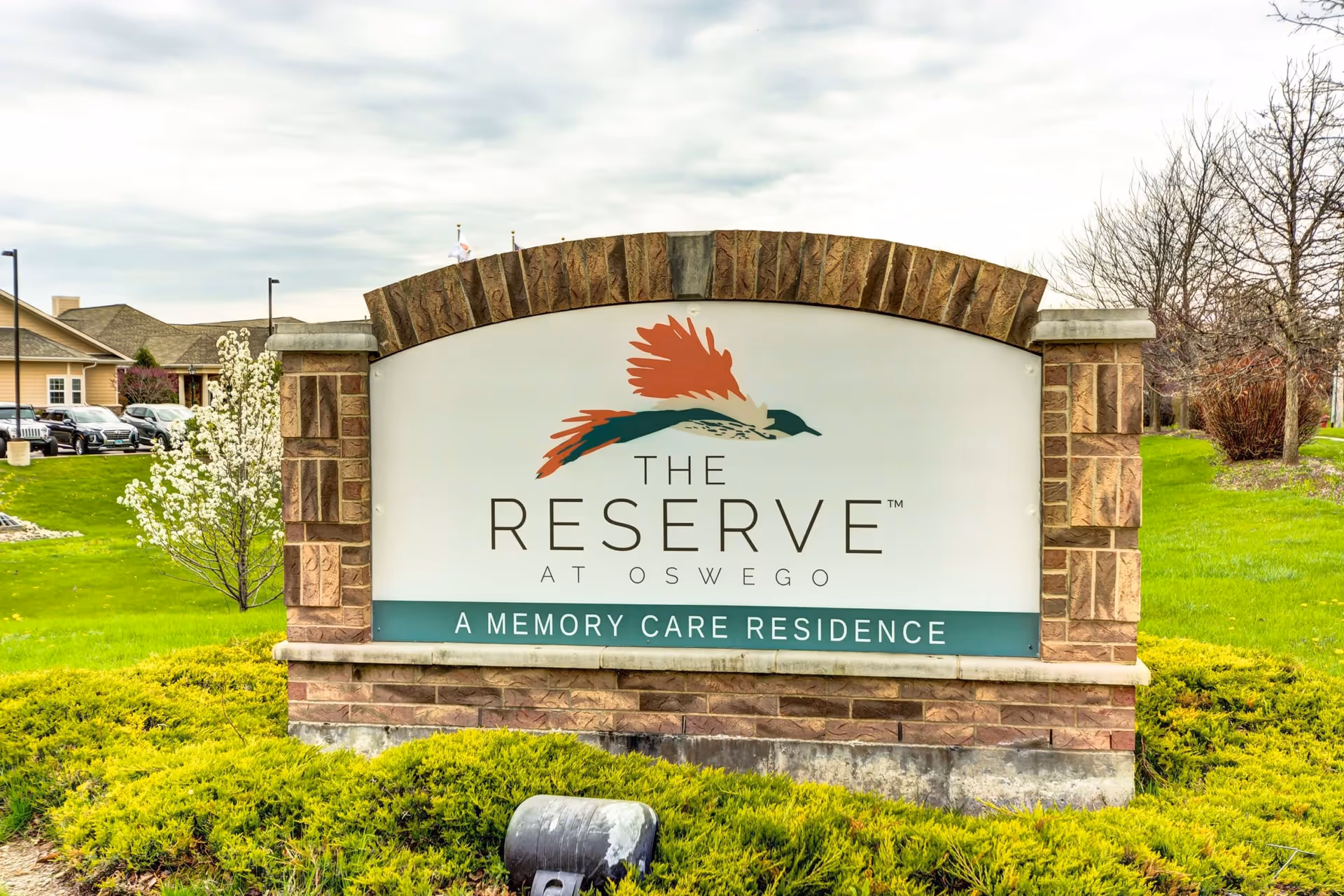 Stone entrance sign reading 'The Reserve at Oswego - A Memory Care Residence' on a landscaped lawn in front of the facility.