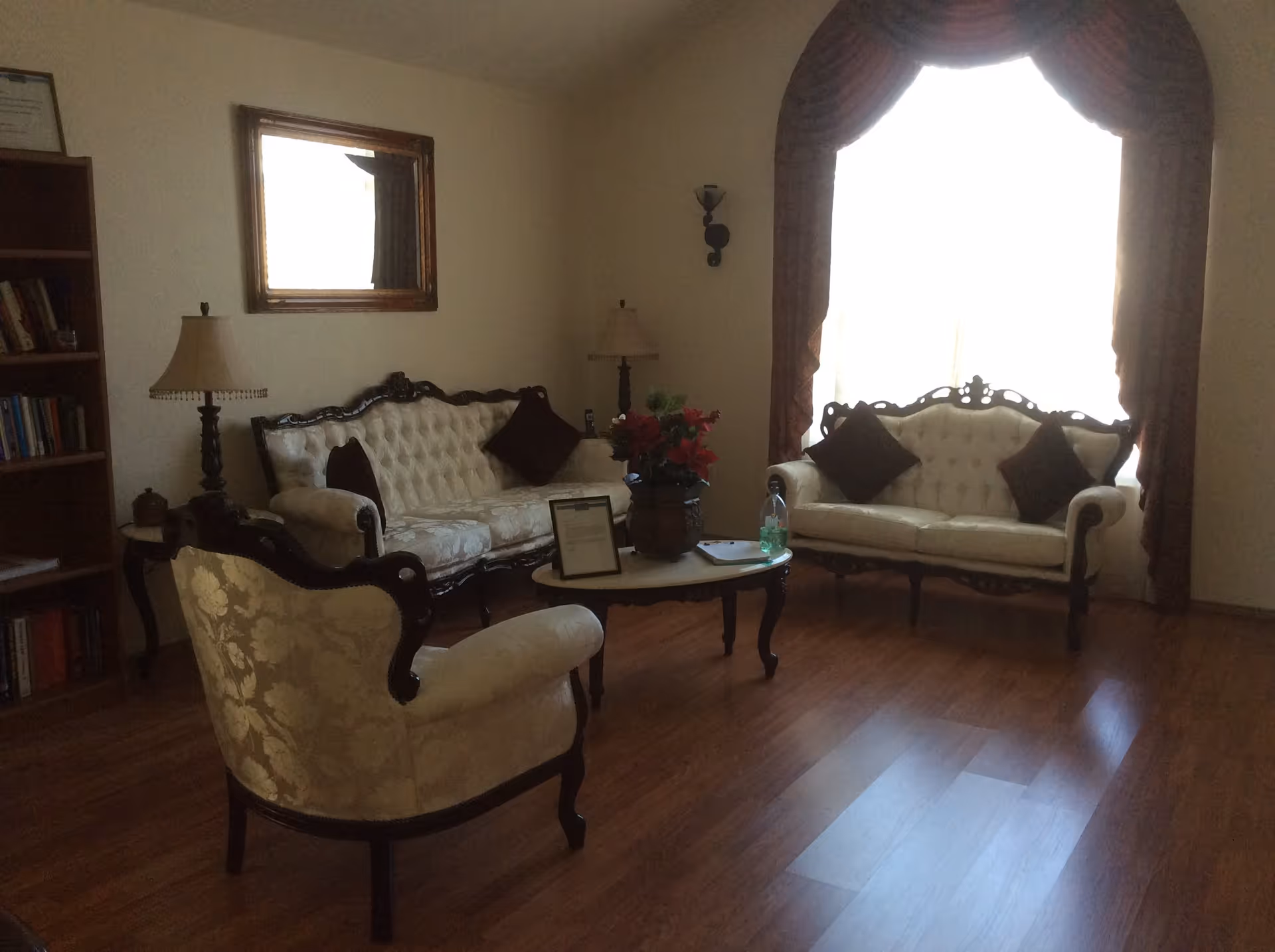 Antique-style living room with tufted sofas and an armchair arranged around a coffee table in front of a large curtained window.