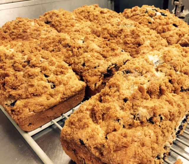 Several freshly baked crumb-topped loaves of bread or cake cooling on a metal rack in a kitchen setting.