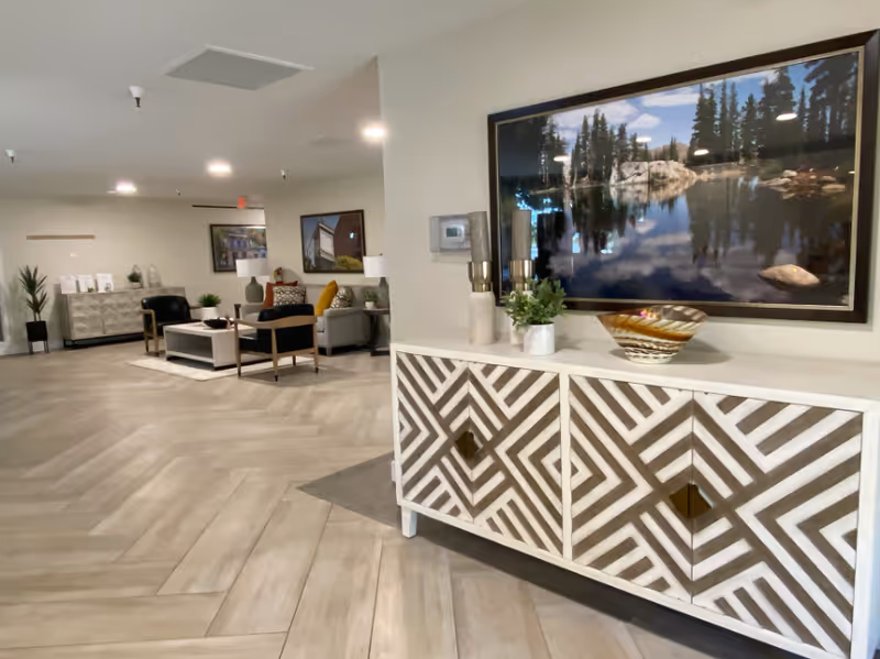 Lobby-style common room with a decorative patterned sideboard, seating area, and a large landscape painting on the wall.