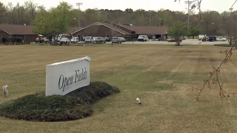 Lawn area with an Open Fields sign and a distant building in the background.
