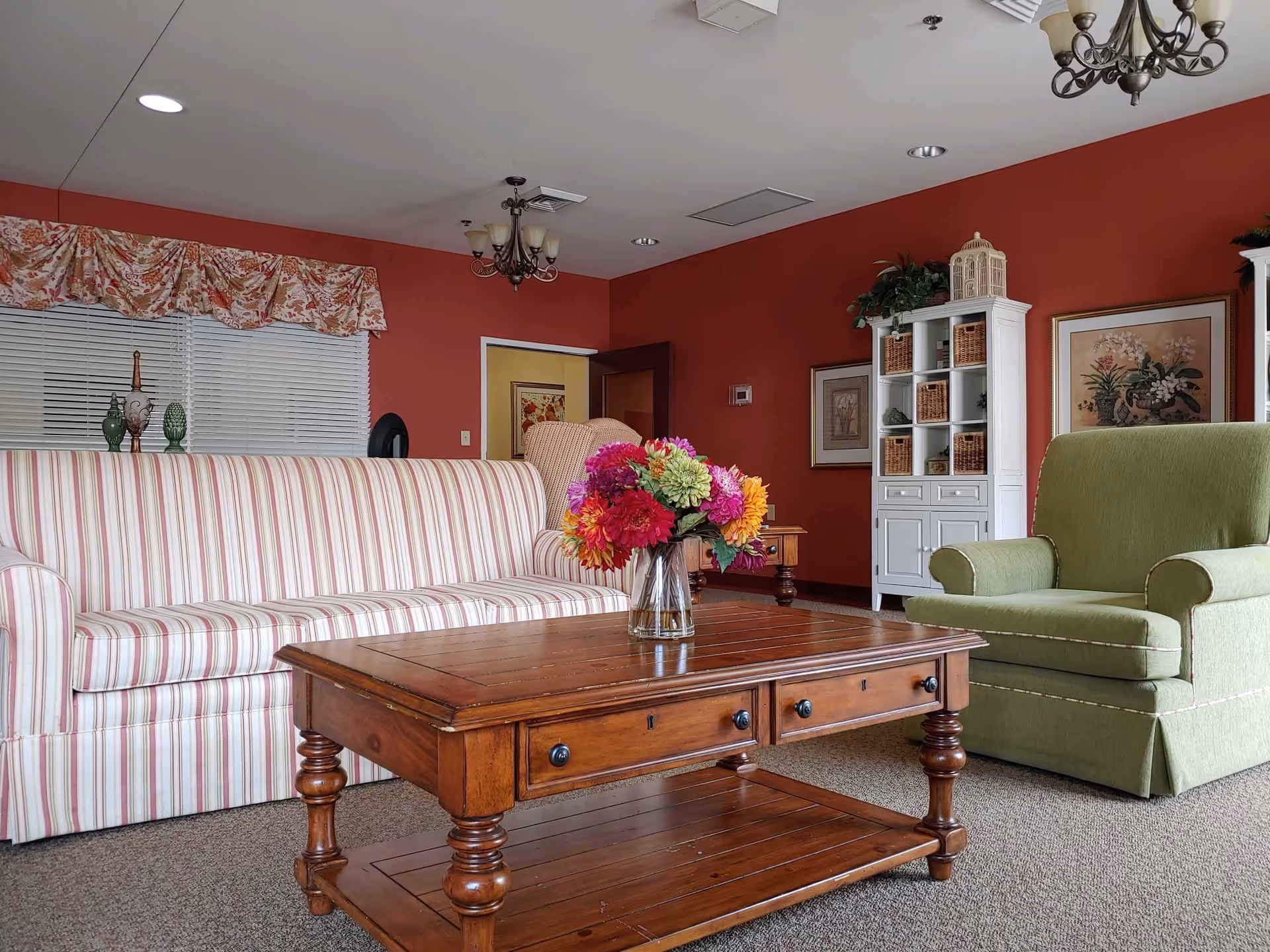 Cozy senior living living room with striped sofa, green armchair, wooden coffee table, and display cabinet.