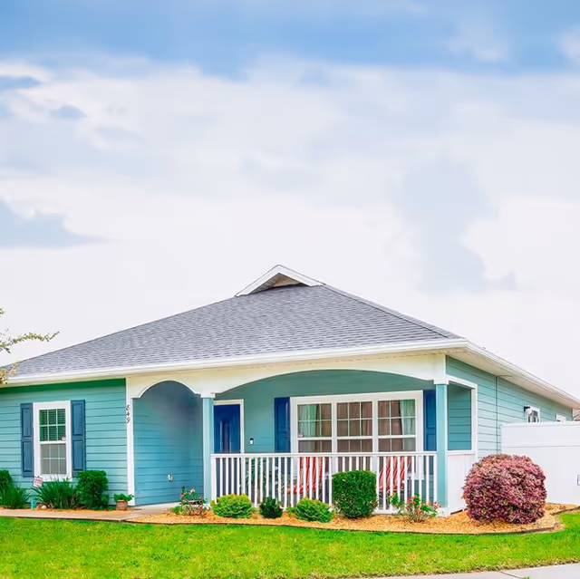 Single-story teal house with a covered front porch, white railing, and landscaped lawn.