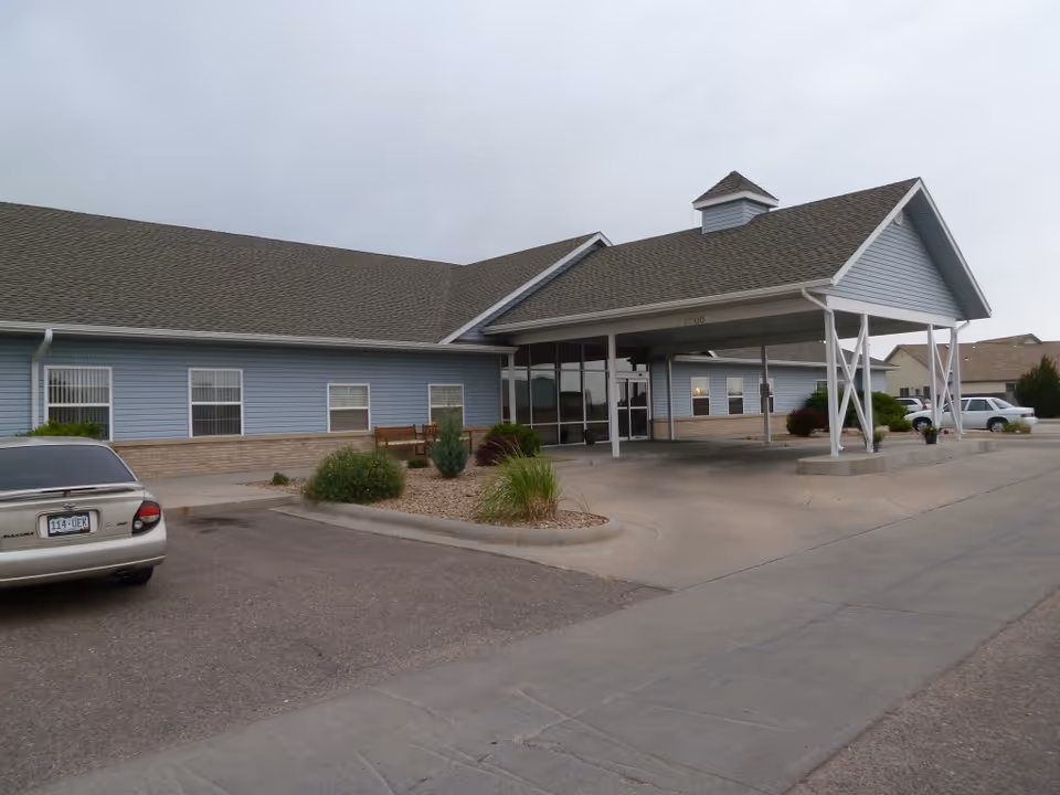 Single-story assisted living building front with a covered entrance/portico, parking area, and landscaping.