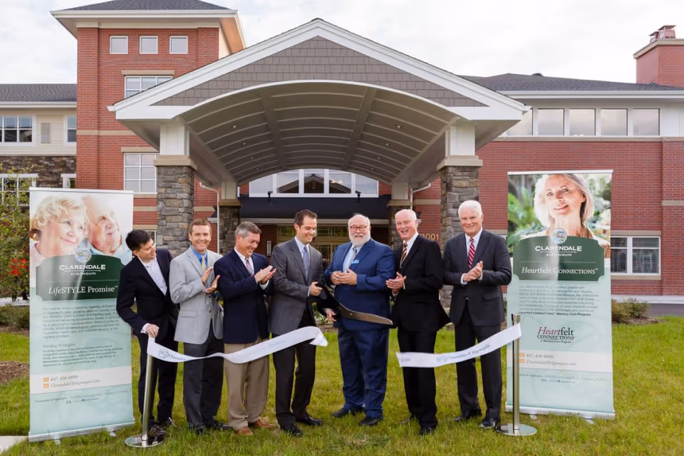 A group of men in suits cutting a ceremonial ribbon in front of the Clarendale of Algonquin building entrance.
