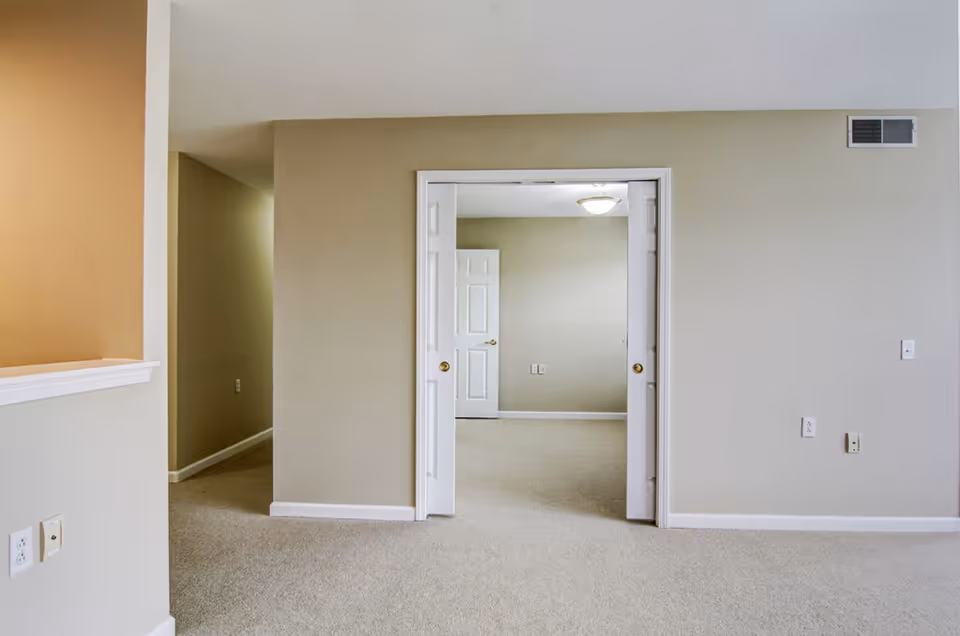 Carpeted neutral-toned interior living area with an open doorway leading to another room.