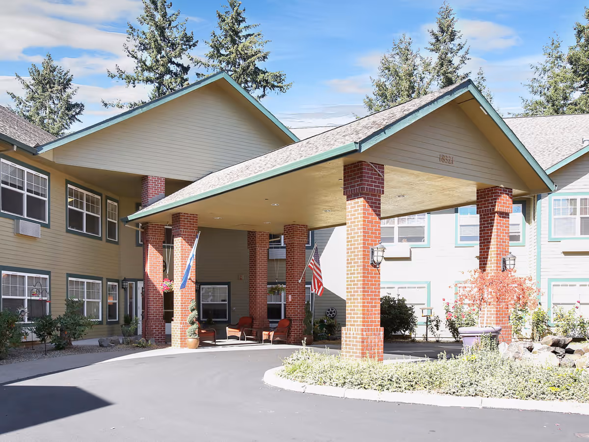 Covered porte-cochere entrance with brick columns at the front of a senior living facility building.