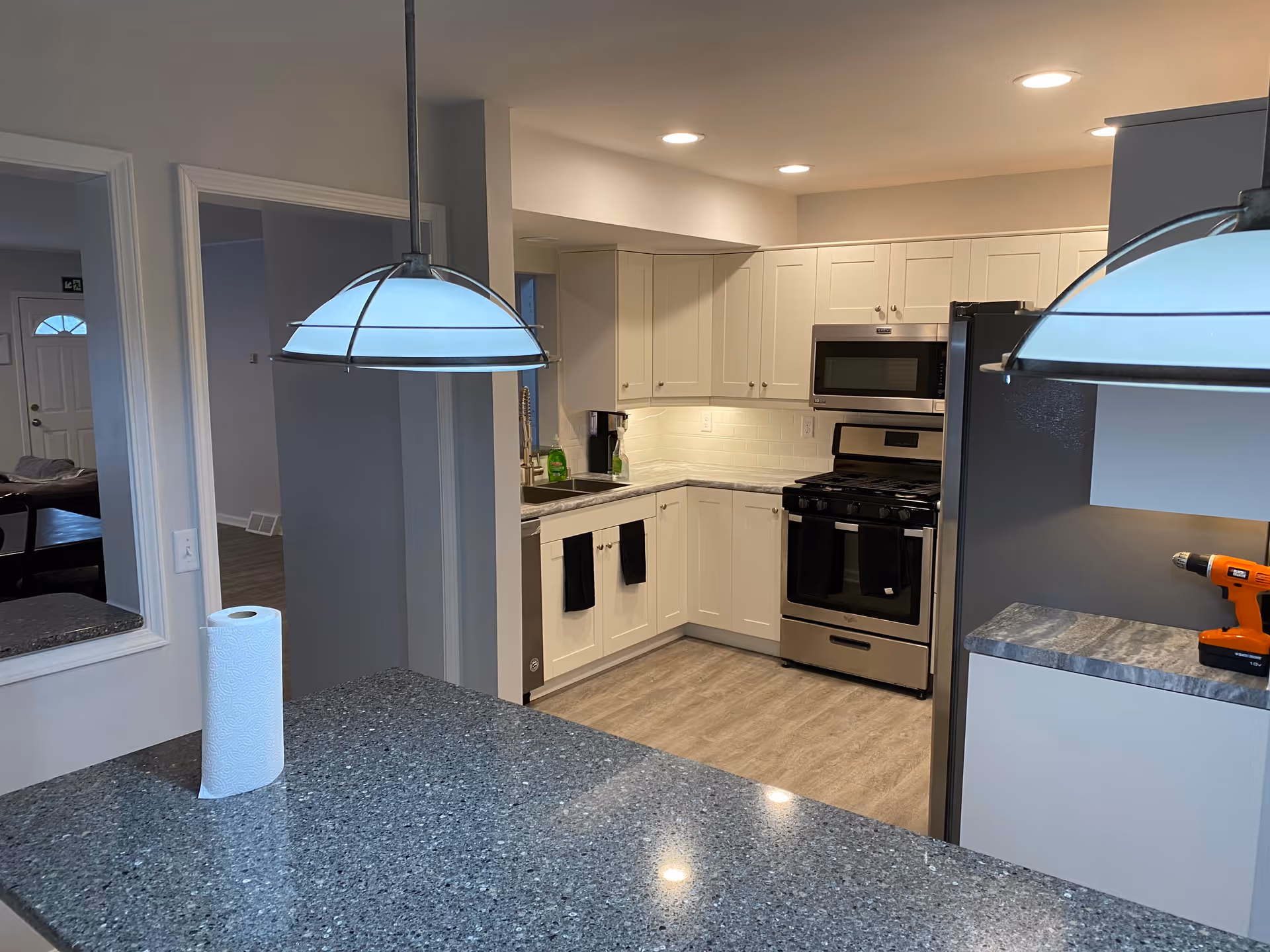 Open kitchen with white cabinets and stainless-steel appliances, a speckled countertop island under pendant lights and a paper towel roll on the counter.