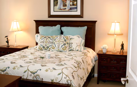 Bedroom with a floral-patterned bed, teal pillows, wooden headboard, matching nightstands with lamps, and framed art above.