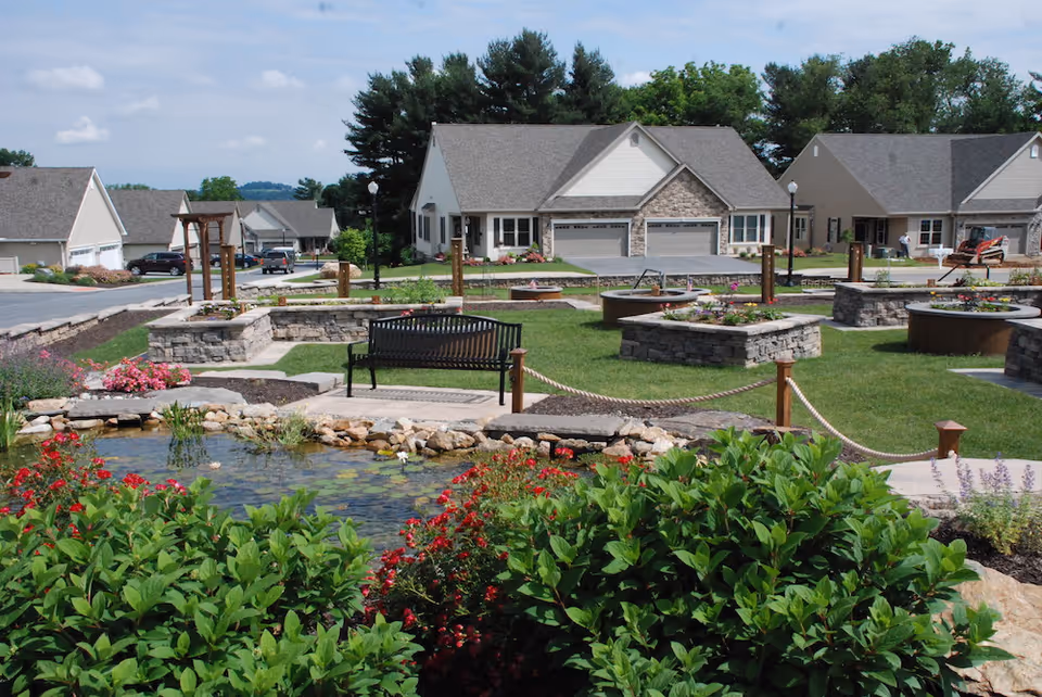 Landscaped courtyard with a small pond, bench, stone planters and residential buildings in the background.