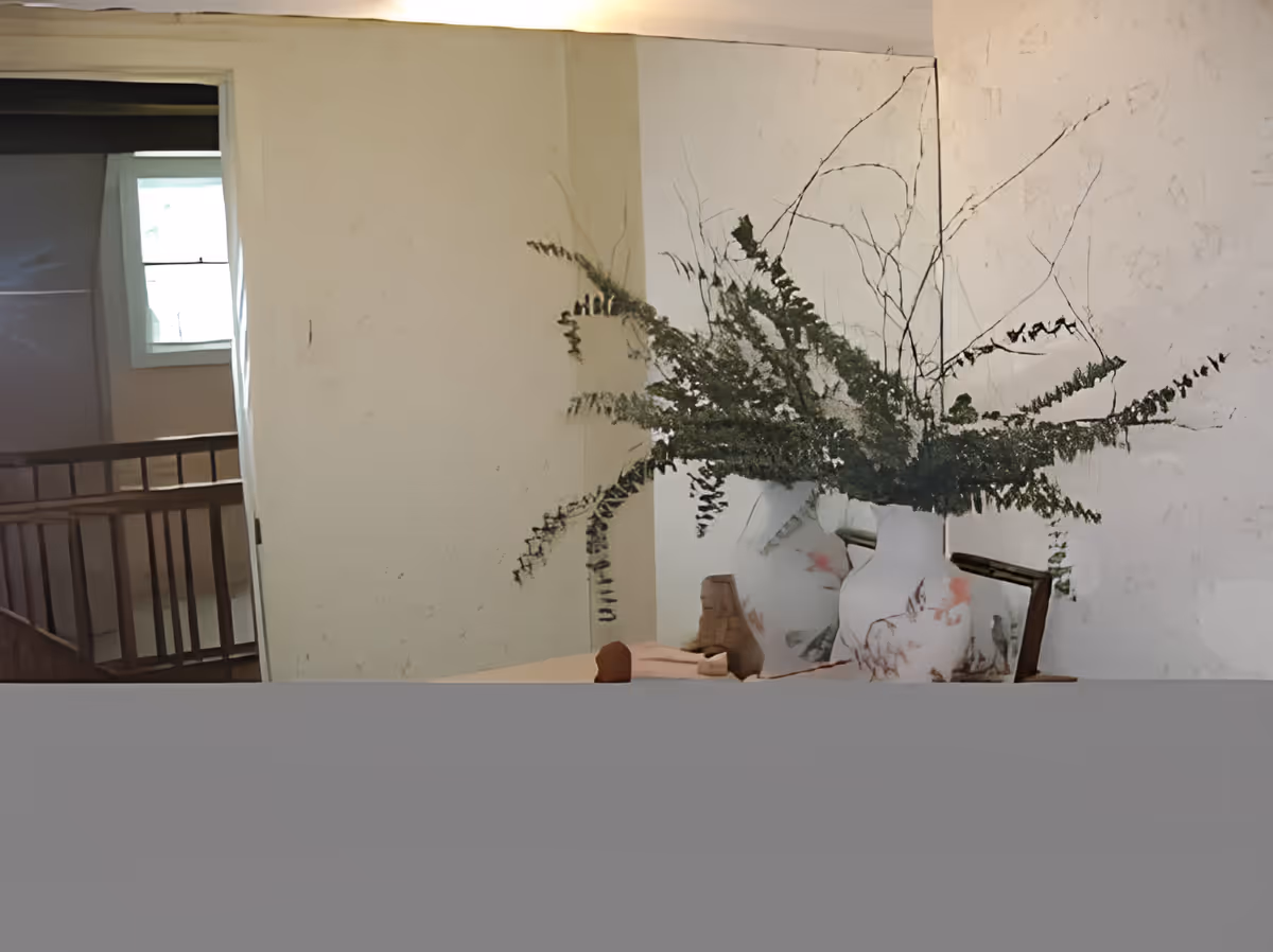 Interior hallway/foyer with a table holding a large floral vase of branches in front of a textured wall and a view into a stairwell and window.