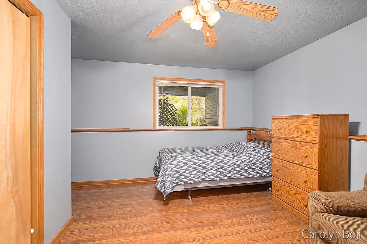 Simple bedroom with a bed, wooden dresser, ceiling fan and hardwood floors.