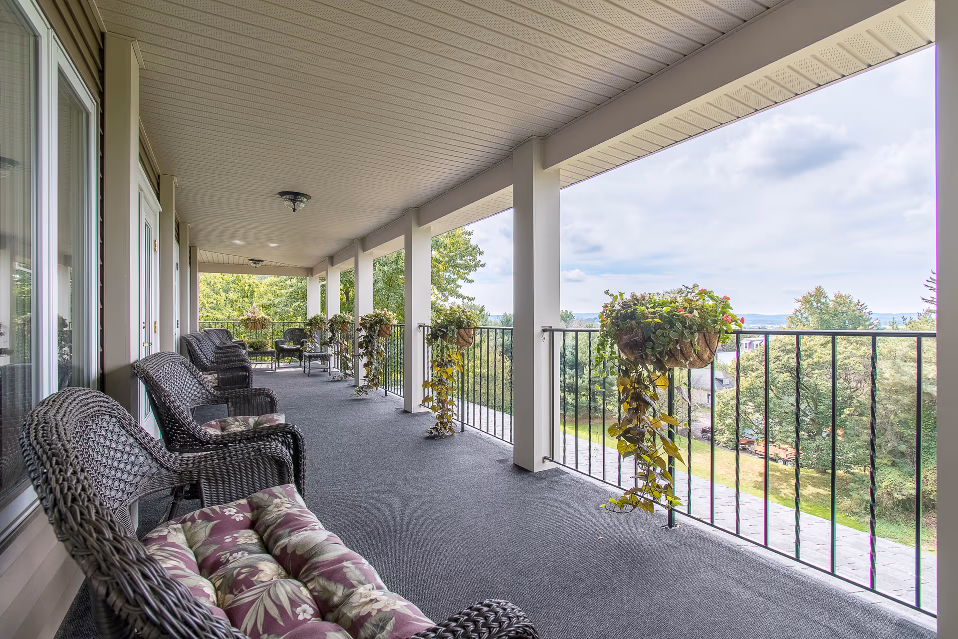 Covered balcony with wicker chairs and hanging planters overlooking a landscaped yard.